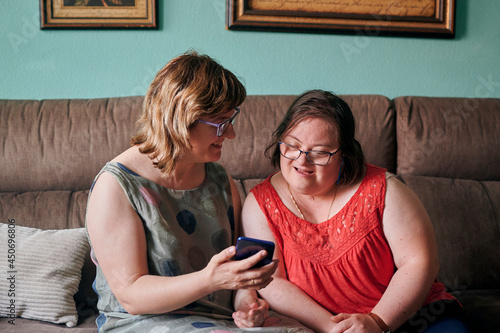 Adult woman and her sister with down syndrome look at a phone at home photo