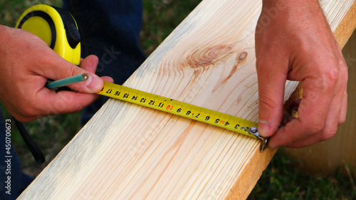 Male carpenter measuring wooden blank with the lines and making marks with a pencil and tape. Close up view.