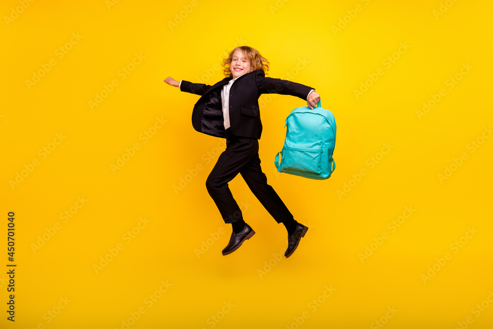 Full size profile side photo of good mood lovely boy running in air hold rucksack education isolated on yellow color background