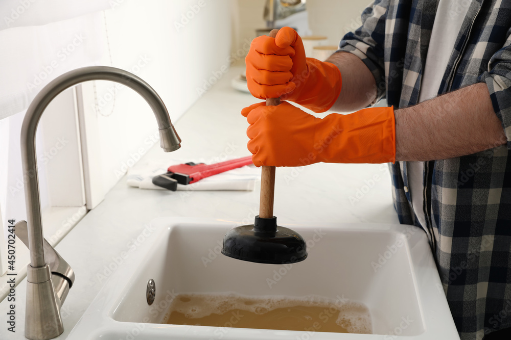Man using plunger to unclog sink drain in kitchen, closeup - obrazy, fototapety, plakaty 