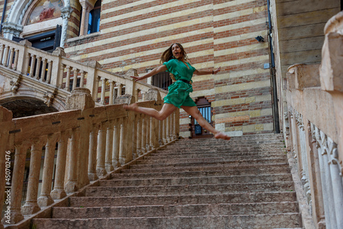 Girl in green casual dress, jumps in dance motion on a staircase outside in the city.