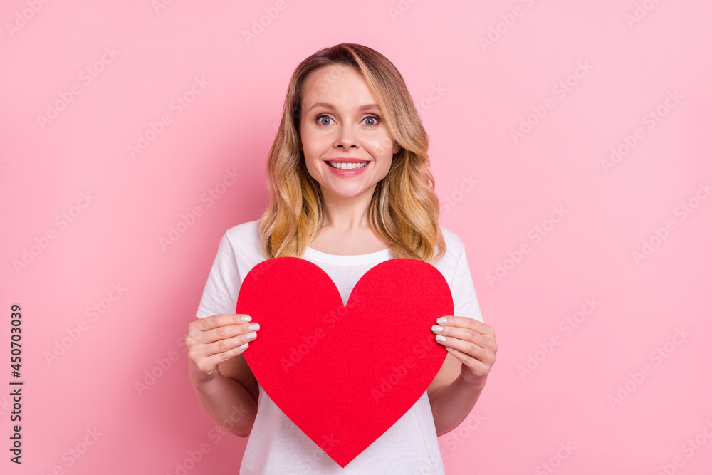 Photo of cheerful young happy woman hold hands big red paper heart smile isolated on pink color background Photo of cheerful young happy woman hold hands big red paper heart smile isolated on pink color background