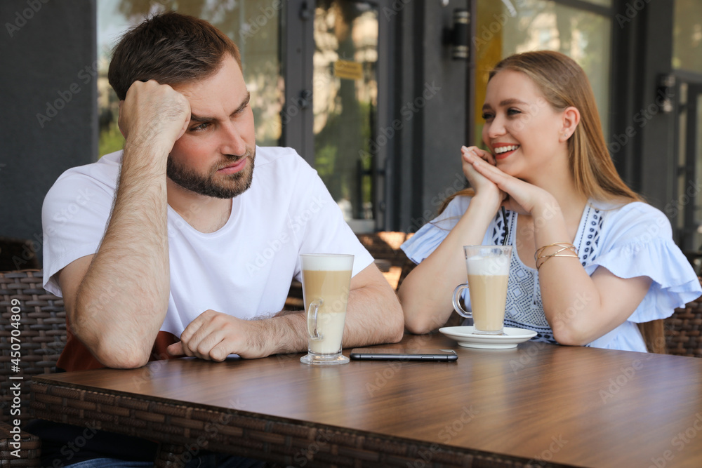 Young man having boring date with talkative girl in outdoor cafe