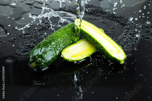 sliced fresh cucumber halves on dark glass with splashing water