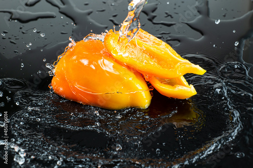 sliced halves of fresh sweet orange peppers on dark glass with splashing water