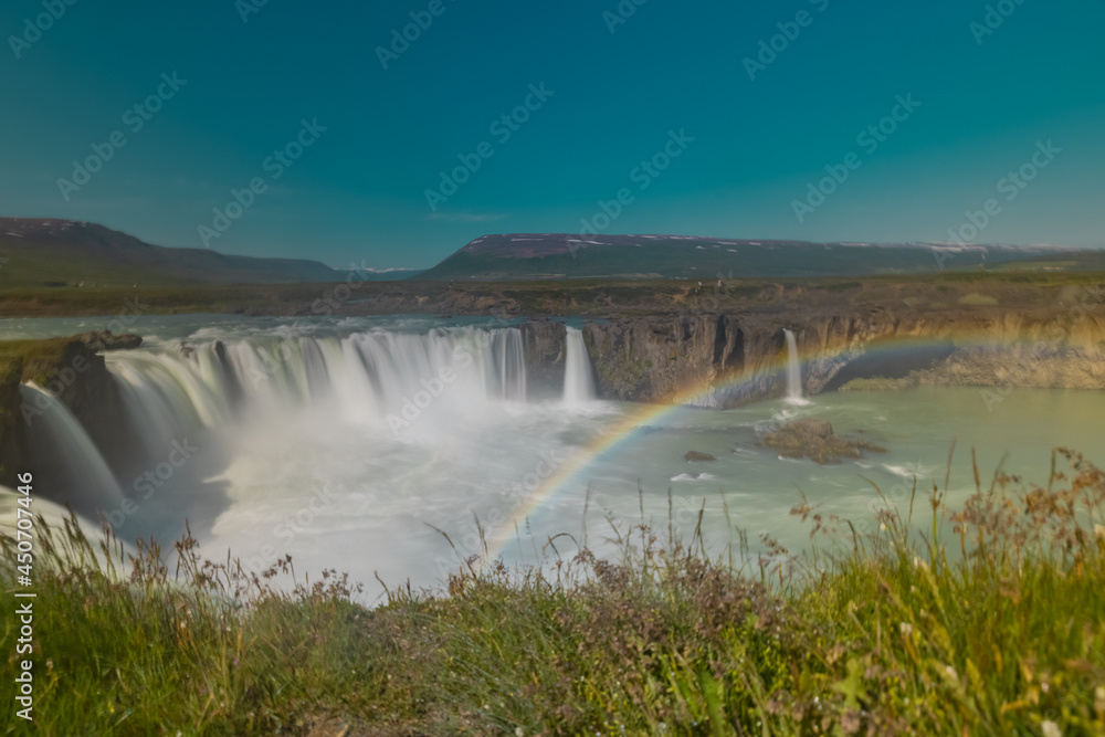 Fototapeta premium Long exposure photo of magnificent Godafoss waterfall in northern Iceland on a warm summer day. Visible rainbow from drops of water coming from the waterfall.