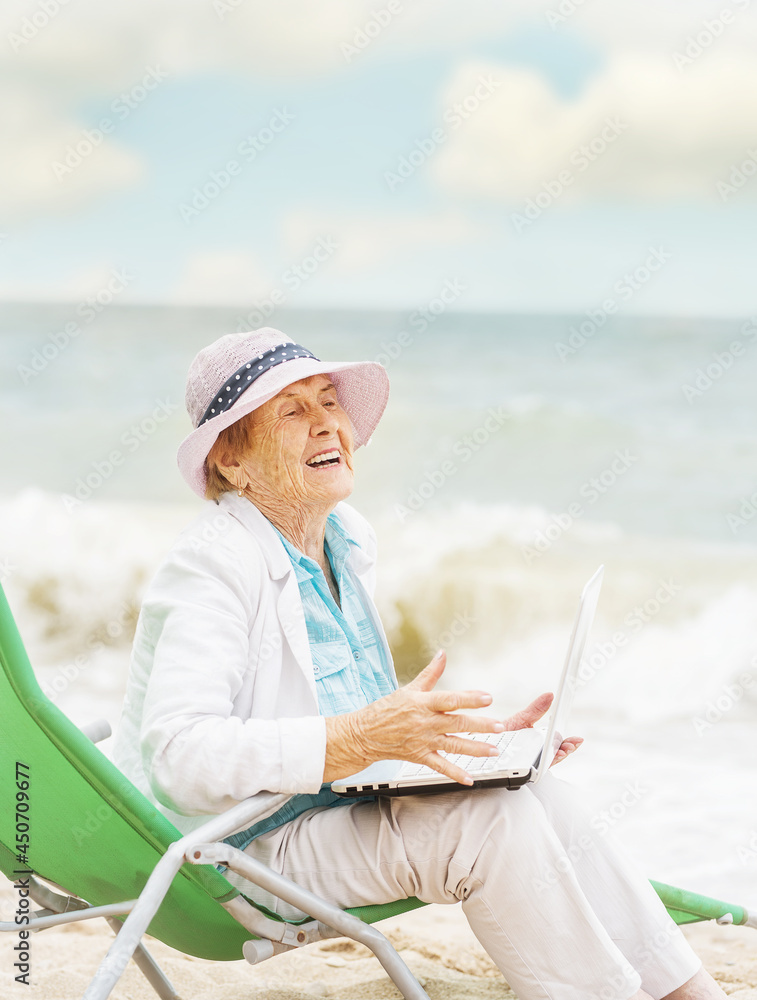 Very old wrinkled woman in a playful mood with a laptop on the seashore.