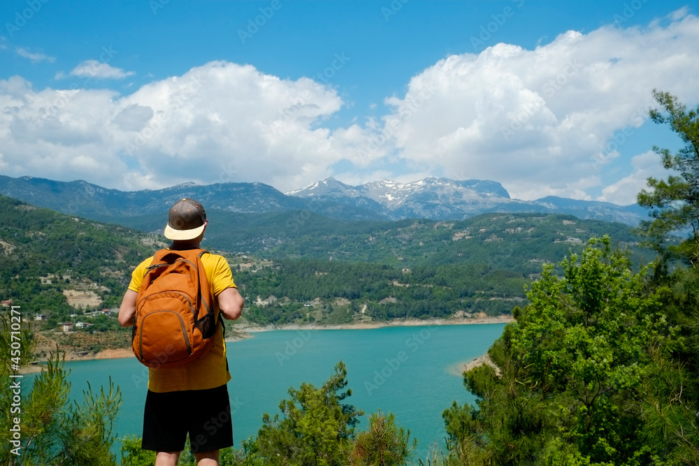 Young man wearing yellow t-shirt and orange backpack enjoying the panoramic view of green hills somewhere in Antalya, Turkey. Dim Cayi mountain river background. Copy space for text.