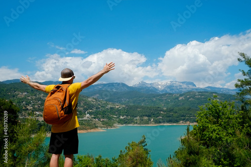 Young man wearing yellow t-shirt and orange backpack enjoying the panoramic view of green hills somewhere in Antalya  Turkey. Dim Cayi mountain river background. Copy space for text.