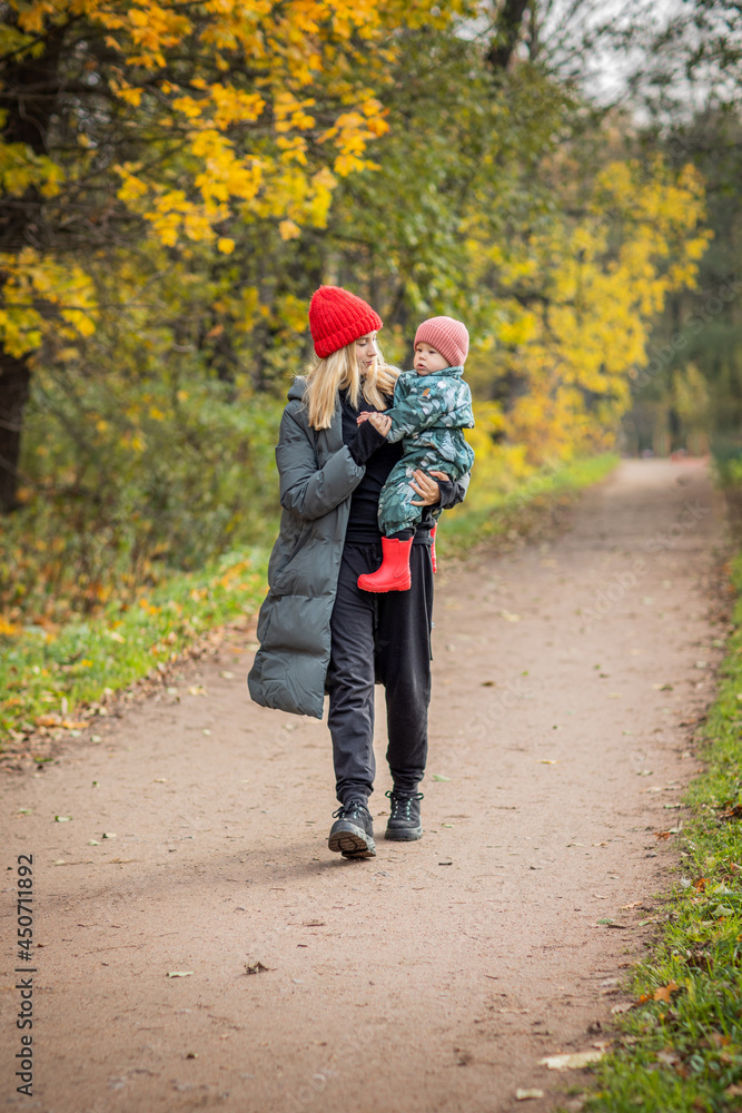 Obraz premium mom and baby on a walk in the autumn park, baby in mom's arms, warm clothes, bright hats