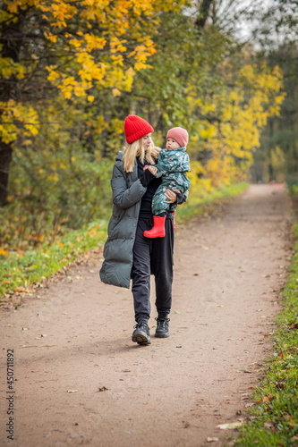 mom and baby on a walk in the autumn park, baby in mom's arms, warm clothes, bright hats © Leka