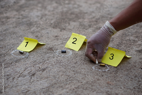  Concept : Crime scene. Hand is drawing circle around bullet shells on the floor to mark crime evidence point and yellow signs with number 1,2,3 . 