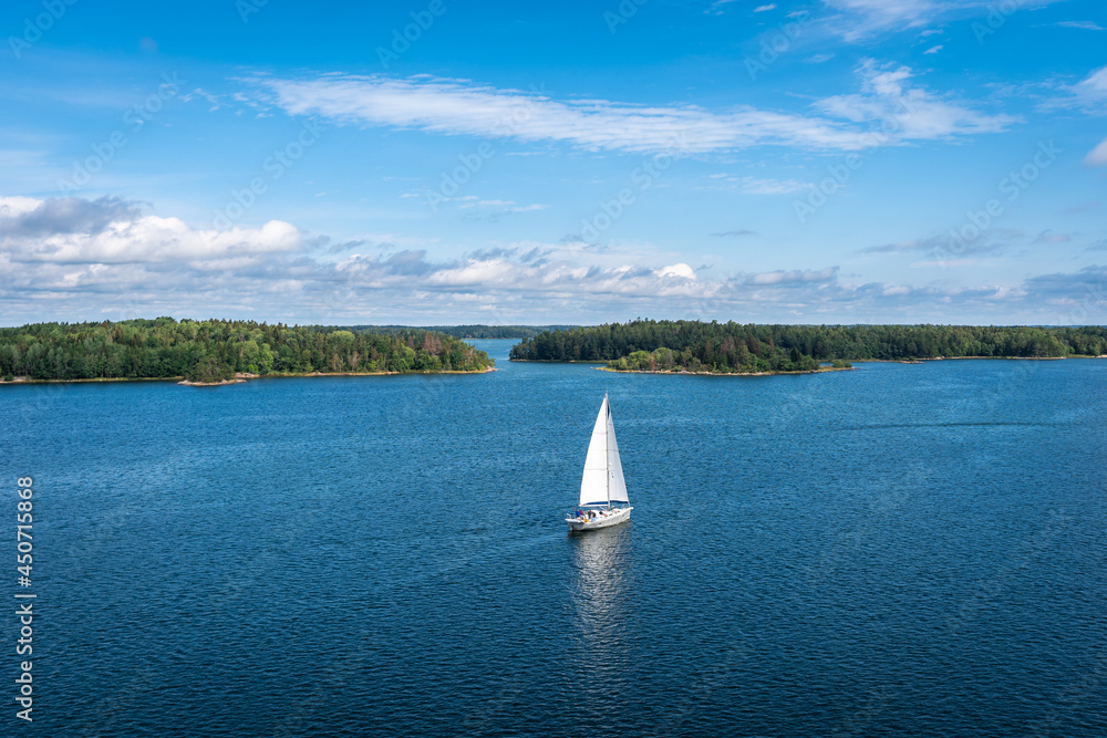 Aerial view of beautiful modern white sailing yacht sails on the sea surface on sunny summer day. Shot from cruise ship. Forest green long coastline Relax water travel trip adventure hobby lifestyle