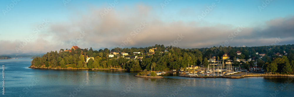 Beautiful view of Stockholm archipelago of the Baltic sea in summer morning. Panorama of the shores of Scandinavia Sweden from cruise ship. Forest green islands and coast with villas and buildings.