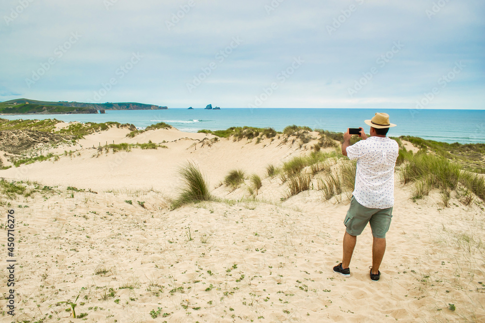 Hombre con sombrero de paja fotografiando con el teléfono movil el parque natural de las dunas de Liencres en Cantabria, España Hombre con sombrero de paja fotografiando con el teléfono movil el parque natural de las dunas de Liencres en Cantabria, España