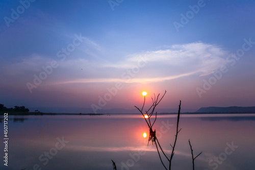 Twilight sunset in the dusk reflection of the water surface, with branches in the foreground,with mountains and the night sky in the background