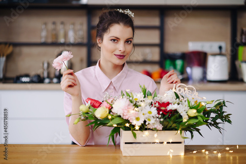 Florist at work: pretty young brunette woman making fashion modern composition of different flowers decorating with led lights at home photo
