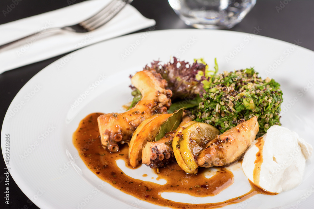 Grilled octopus with quinoa salad on a white porcelain plate.