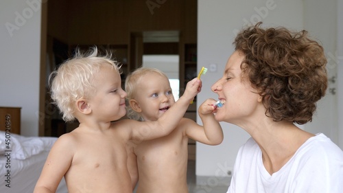 Strategies for how to make brushing teeth fun: young mom lets her twin babies to brush her teeth 