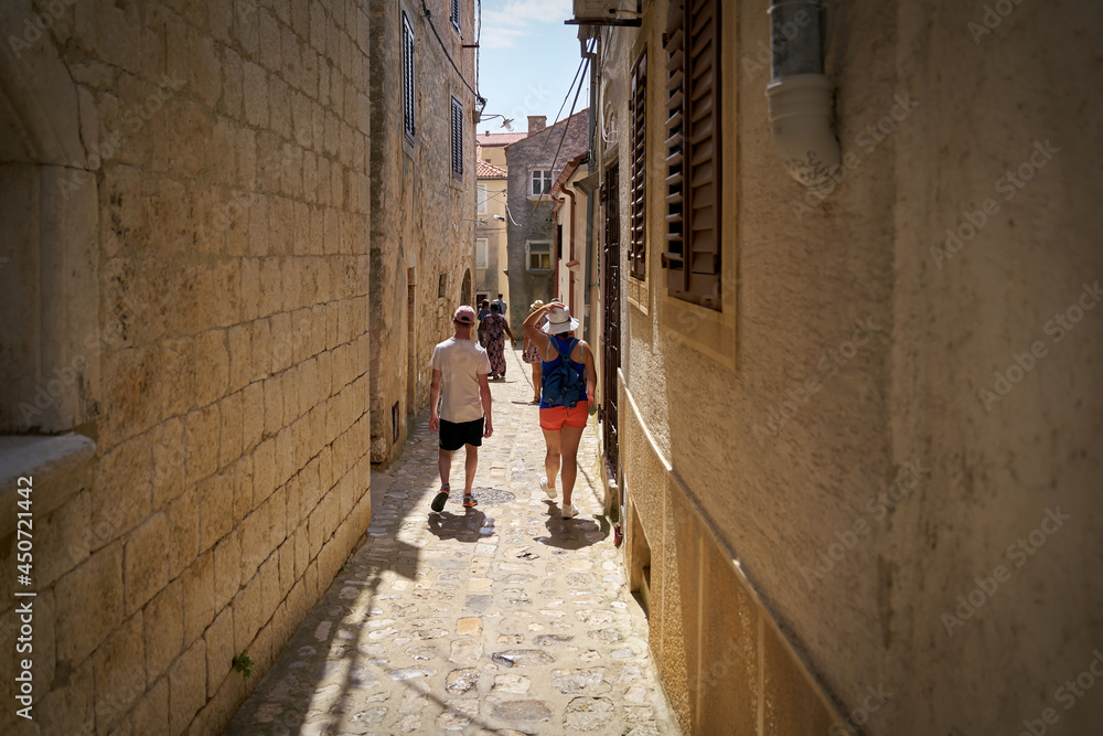 Tourists in a narrow alley in the old town of Krk on the island of the same name in Croatia on a hot summer day