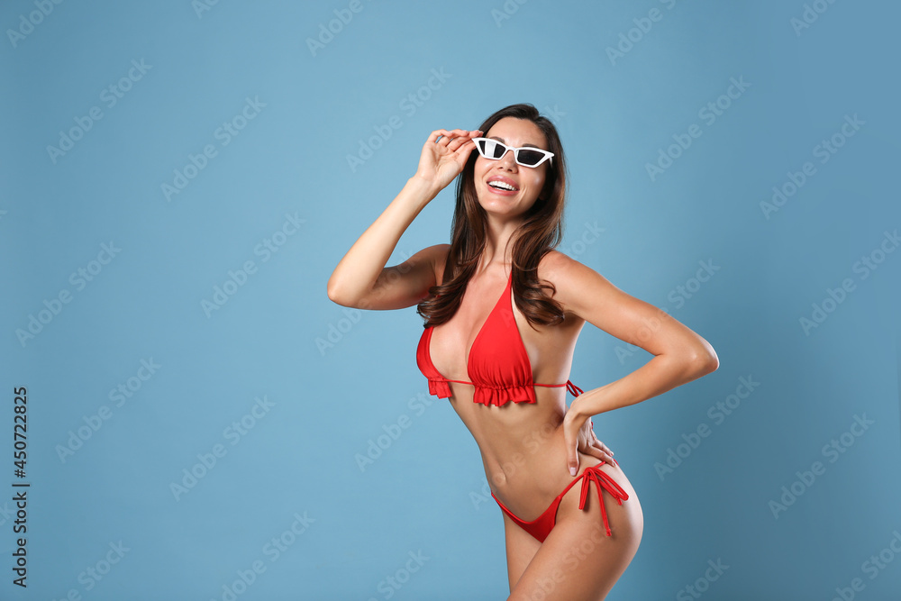 Obraz premium Beautiful woman in stylish bikini and sunglasses on blue background. Space for text