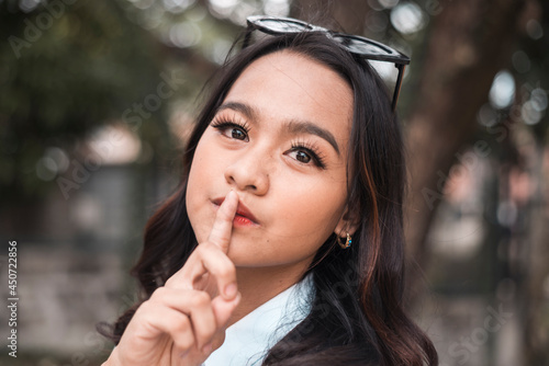 A young asian lady request someone to keep quiet in a polite but stern way. Outdoor scene.