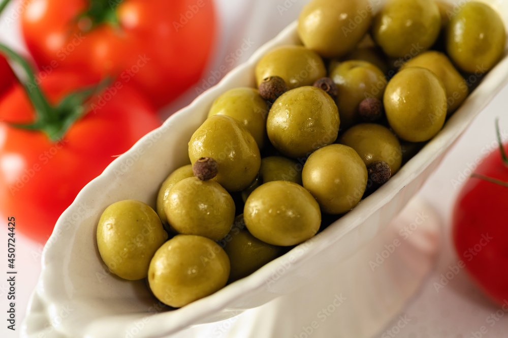 green olives in decorative dishes with red tomatoes on a white background, large format