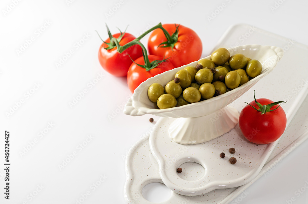 green olives in a decorative dish with red tomatoes on a white background, empty space for text