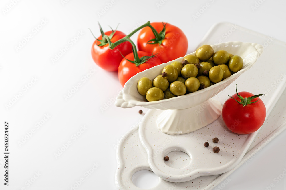 green olives in a decorative dish with red tomatoes on a white background, empty space for text green olives in a decorative dish with red tomatoes on a white background, empty space for text