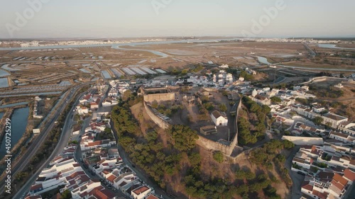 Aerial drone flying over hilltop Castelo de Castro Marim Castle, village settlements and salt flats.