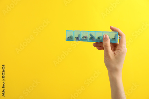 Woman holding plastic box with different pills on yellow background, closeup. Space for text