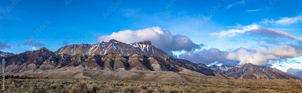 A panorama of distant snow covered mountain peaks with white clouds and blue skies in Idaho.