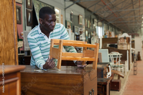 African American man looking for vintage wooden furniture in furnishings store.. © JackF