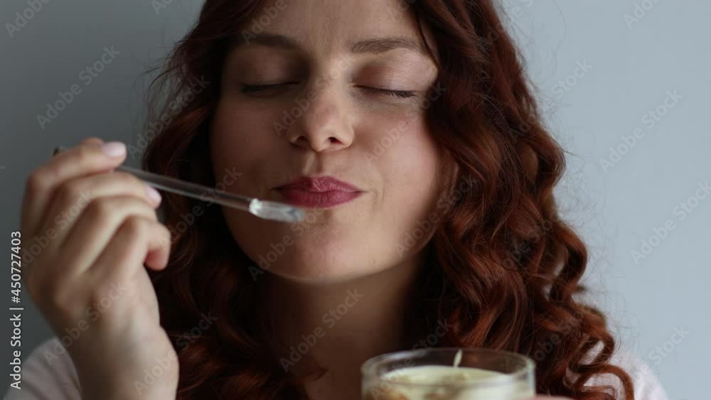 Close-up portrait of positive curly haired caucasian girl eating delicious creamy dessert, enjoying taste on gray background Close-up portrait of positive curly haired caucasian girl eating delicious creamy dessert, enjoying taste on gray background