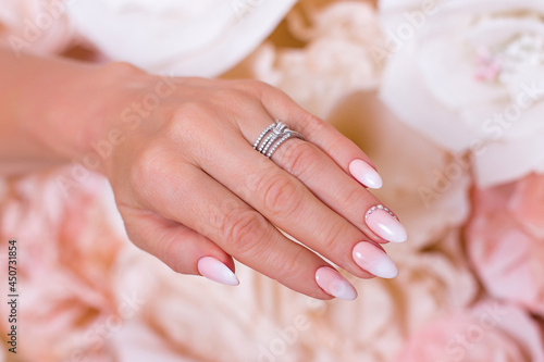 Female hand with ombre manicure nails, pink gel polish, on paper flowers background