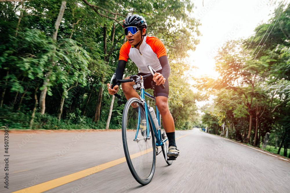Obraz premium A man ride on bike on the road. Man riding vintage sports bike for evening exercise. A man ride bicycle to breathe in the fresh air in midst of nature, meadow, forest, with evening sun shining through