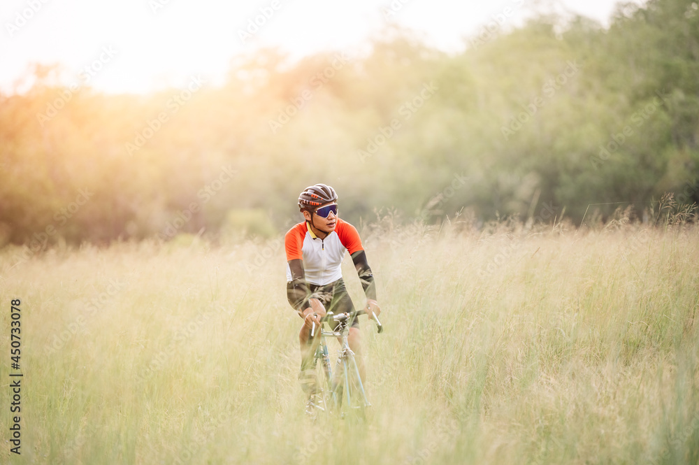 A man ride on bike on the road. Man riding vintage sports bike for evening exercise. A man ride bicycle to breathe in the fresh air in midst of nature, meadow, forest, with evening sun shining through A man ride on bike on the road. Man riding vintage sports bike for evening exercise. A man ride bicycle to breathe in the fresh air in midst of nature, meadow, forest, with evening sun shining through