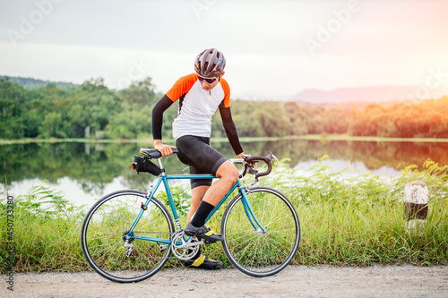 Fototapeta Naklejka Na Ścianę i Meble -  A man ride on bike on the road. Man riding vintage sports bike for evening exercise. A man ride bicycle to breathe in the fresh air in midst of nature, rivers, forest, with evening sun shining through