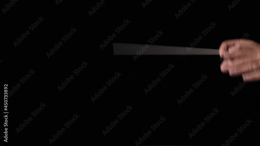 The hands of an orchestra director, using his baton to synchronize the musicians while they play music. Black background, profile detail shot, plenty of space on the left. The hands of an orchestra director, using his baton to synchronize the musicians while they play music. Black background, profile detail shot, plenty of space on the left.