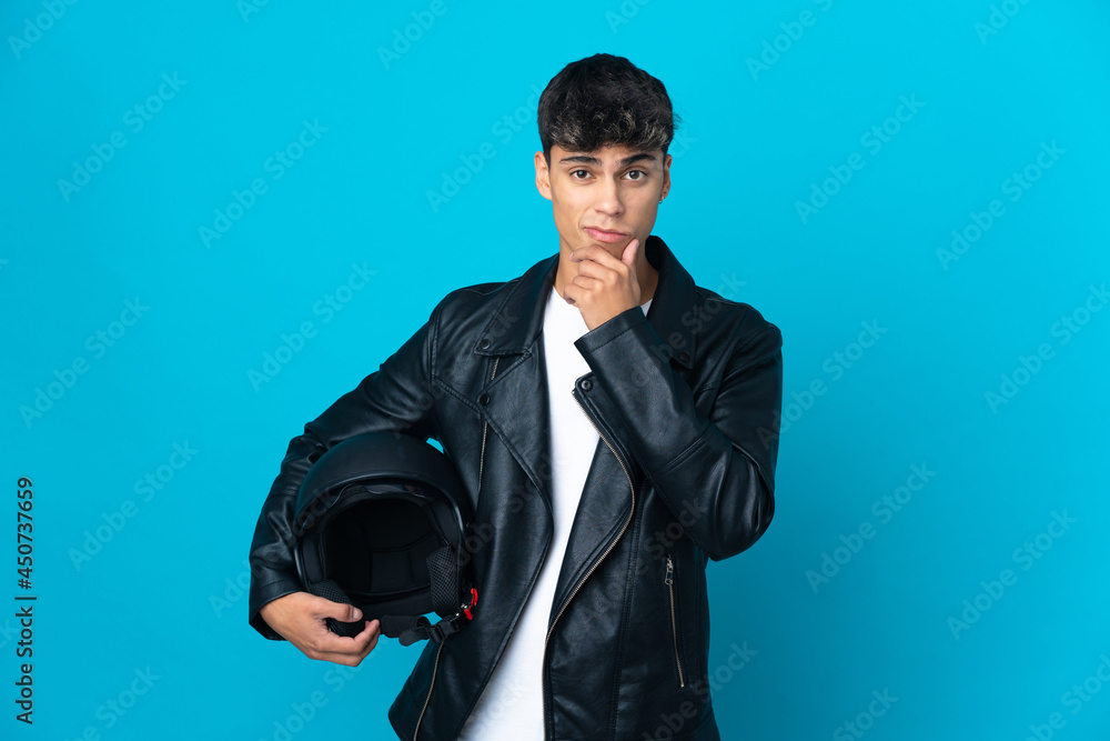 Young man with a motorcycle helmet over isolated blue background thinking Young man with a motorcycle helmet over isolated blue background thinking