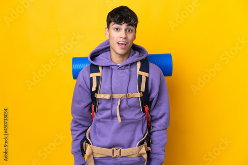 Young mountaineer man with a big backpack over isolated yellow background with surprise facial expression