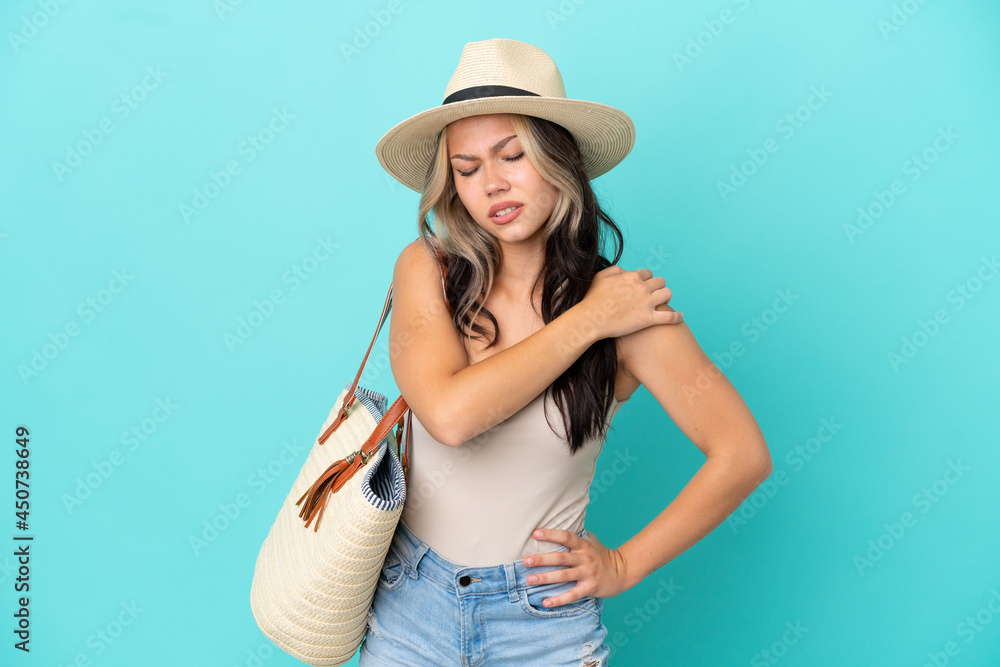 Teenager Russian girl with pamel and beach bag isolated on blue background suffering from pain in shoulder for having made an effort Teenager Russian girl with pamel and beach bag isolated on blue background suffering from pain in shoulder for having made an effort