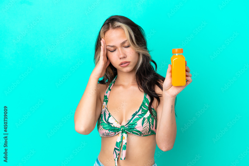 Teenager Russian girl in swimsuit drinking orange juice isolated on blue background with headache Teenager Russian girl in swimsuit drinking orange juice isolated on blue background with headache