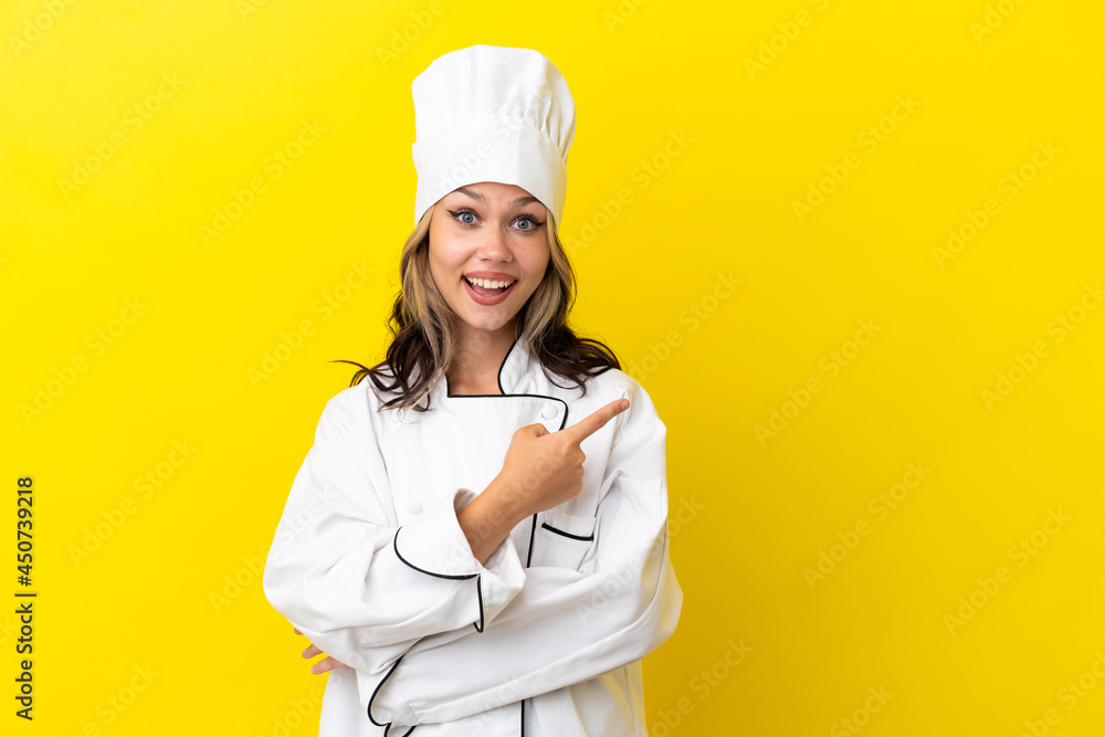 Young Russian chef girl isolated on yellow background surprised and pointing side Young Russian chef girl isolated on yellow background surprised and pointing side