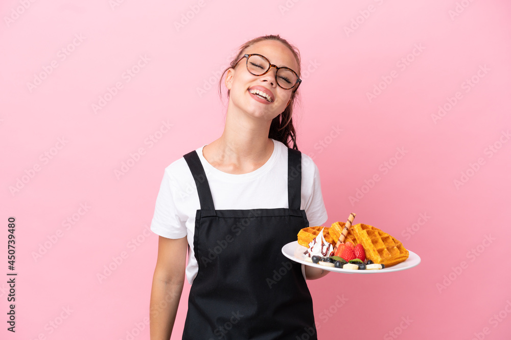 Restaurant waiter Russian girl holding waffles isolated on pink background laughing Restaurant waiter Russian girl holding waffles isolated on pink background laughing