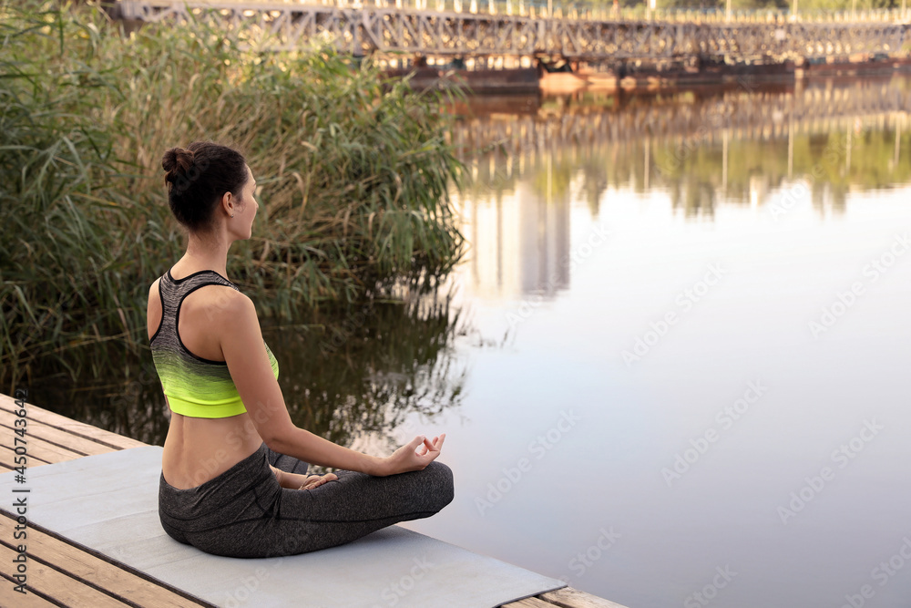 Woman meditating on wooden pier near river. Space for text