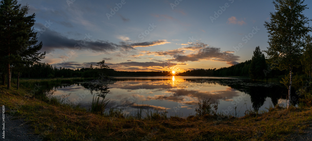 panorama of a colorful sunset reflected in a calm lake landscape with green forest and reeds