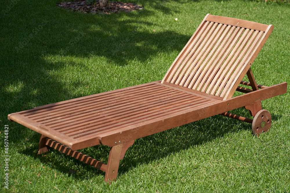 Wooden chaise longue in the fresh garden on the green grass. The shadow of a tree on the grass.The concept of recreation, tanning in the backyard. High quality photo Wooden chaise longue in the fresh garden on the green grass. The shadow of a tree on the grass.The concept of recreation, tanning in the backyard. High quality photo