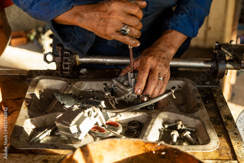 A man, who works as a mechanic, skillfully fixes the carburetor of a boat engine in his workshop photo