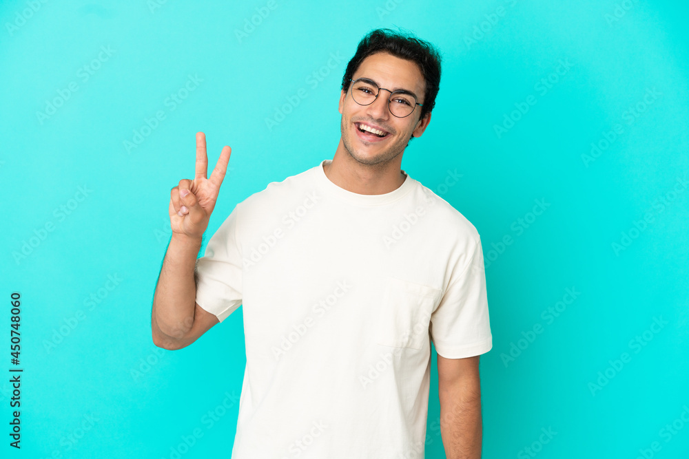 Fototapeta premium Caucasian handsome man over isolated blue background smiling and showing victory sign